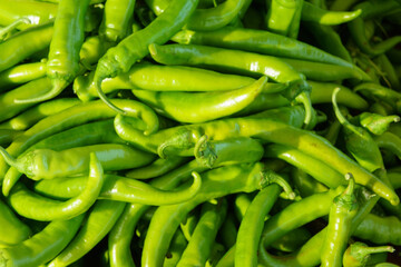 A close-up shot of vibrant green chili peppers piled high at a farmers market