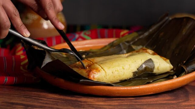 Hands of a Mexican woman cutting a piece of banana leaf tamale with cutlery