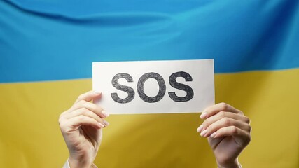 Female hands with SOS, alarm, emergency card on Ukrainian National flag background. Ukraine labor exploitation, war, invasion, human resources, request for help, environmental care - Powered by Adobe