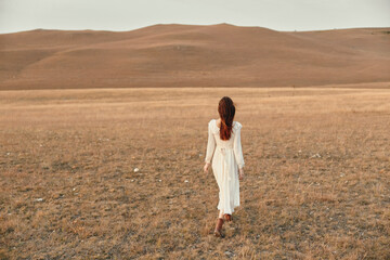 Woman in white dress walking through open field in daylight beauty and serenity of nature fashion and gracefulness of woman's movement