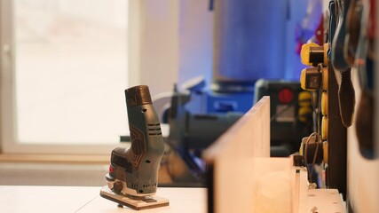 Close up of electric router on workbench in assembly shop with woodworking tools on rack in background. Focus on hand powered gear used for cutting wood in carpentry studio, panning shot