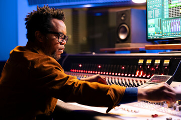 Professional audio technician recording and editing songs by adjusting volume levels with...