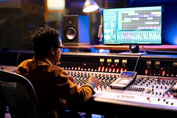 African american sound designer uses mixing console with knobs and faders in control room, editing...