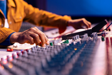 African american sound designer twisting knobs to edit songs in studio, operating control board...