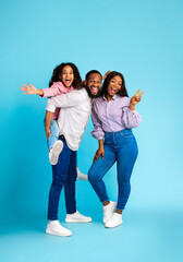 Fototapeta premium Spending Time With Family Is Fun. Full body length of excited African American man, woman and girl laughing and posing isolated over yellow studio wall. Cheerful father carrying his daughter on back