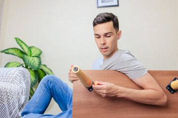 Man attaching a wooden leg to a table in the living room as part of a DIY home decor and furniture...