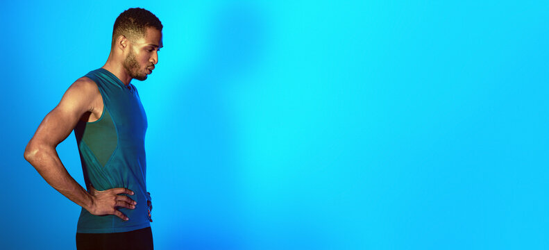 Black Man In Sportswear Doing Breathing Exercise Getting Ready For Workout Standing On Blue Studio Background. Empty Space, Neon Lights