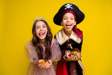 Portrait of two small kids halloween princess pirate costume show tongue hold marmelade isolated on yellow color background