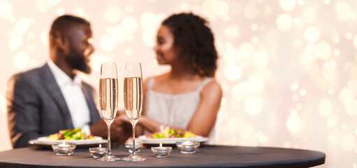 Two glasses of champagne on festive dinner table, black couple having dinner at restaurant