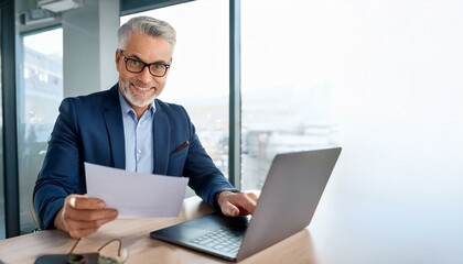 Fototapeta premium Happy busy older professional businessman entrepreneur using laptop holding bill corporate document in office. 50 years old man executive manager or business owner reading paper working on compute