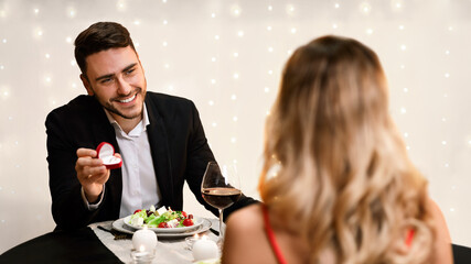 Marry Me. Handsome Guy Making Proposal To His Girlfriend On Romantic Date In Restaurant, Presenting Box With Diamond Ring, Selective Focus