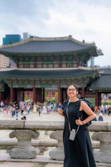 Young happy Latina woman in a black dress admiring the traditional architecture in Gyeongbokgung Palace in Seoul, South Korea.