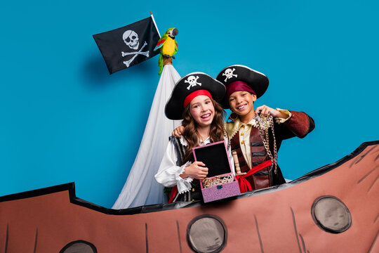 Photo of two small kids hold treasure halloween pirate costume sail ship isolated on blue color background - Powered by Adobe