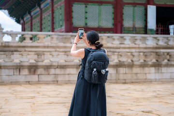 Unrecognizable young Latina woman in a black dress and backpack taking photos at Gyeongbokgung Palace, Seoul, South Korea.