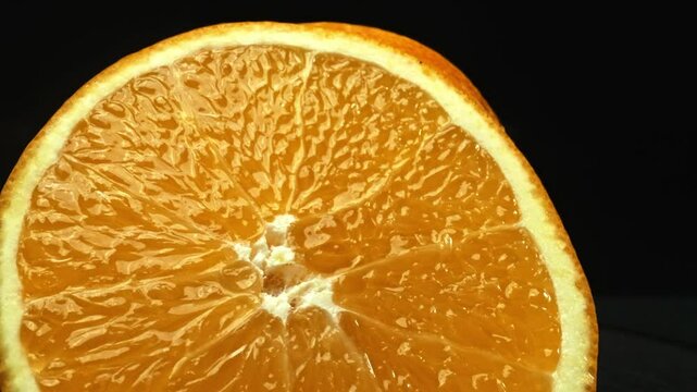 A Macrography capture of an orange slice, placed against a sleek, isolated black backdrop, unfolds as a visual masterpiece of citrus allure. A slice of orange with black background. Comestible.