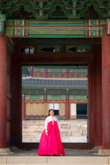 Naklejka premium Happy young Latina dressed in a traditional pink and white hanbok, at Changgyeonggung Palace entrance in Seoul, South Korea.