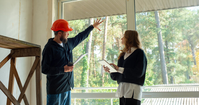 worker in a helmet and customer architect at a construction site inspect plan calculate construction repair. male builder repairman and female boss client in a house under construction use a tablet