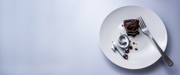 Candles in the shape of the number 19 on plate with piece of cake and fork on grey background. Birthday celebration or after party banner. Selective focus, copy space