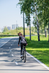 Rear view of Caucasian woman riding bike in park. Vertical photo. 