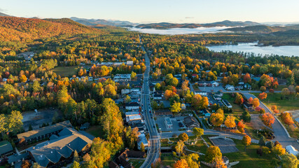 Aerial view of Schroon Lake, NY, with vibrant autumn colors, tree-lined streets, and surrounding Adirondack Mountains, showcasing the small town's scenic charm and peaceful lakeside setting.