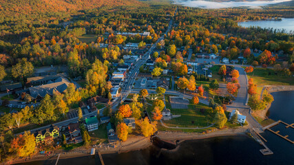 Aerial view of Schroon Lake, NY, highlighting the charming small town, vibrant autumn trees, and peaceful lakeside setting under the warm golden light of late afternoon.