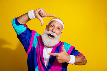 Naklejka premium Photo of cheerful positive mature guy dressed retro sport jacket showing photo gesture emtpy space isolated yellow color background