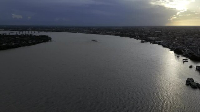 Drone flies over Suriname River toward Jules Wijdenbosch Bridge and De Goslar shipwreck at sunset in Paramaribo, Suriname