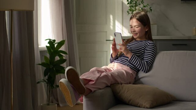 Little girl sitting on sofa mobile phone user smartphone cellphone technology gadget network social media online watching video funny laughter humor tapping cyberspace child home device browse website