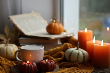 Cup of coffee, pumpkins, burning candles and soft sweater on table. Autumn atmosphere