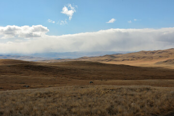 Low cumulus clouds over a hilly dry steppe on a sunny autumn day.