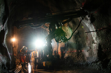 Two miners working in a dimly lit underground tunnel with mining equipment