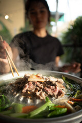 Close up of Asian woman eating Moo Kra Ta or Thai BBQ buffet.