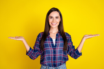 Photo portrait of pretty young girl hand hold compare empty space wear trendy plaid outfit isolated on yellow color background