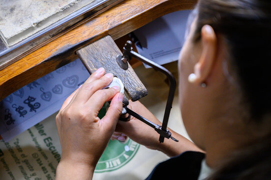 Jeweler cutting a metal object with a saw in her workshop