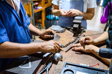 Goldsmith working on precious metal with students carefully watching him in his workshop