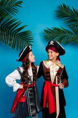 Vertical photo of two small kids cuddle halloween pirate costume isolated on blue color background