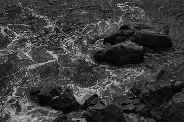 Rocky coastline, black and white with crashing waves textured rocks solid black background intense