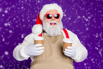 Close-up portrait of nice glad cheerful cheery bearded Santa Claus holding in hands two cups hot cacao sharing with friend isolated over bright vivid shine vibrant violet lilac background