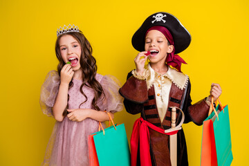 Portrait of two little kids halloween princess pirate costume eat candy hold bags isolated on yellow color background