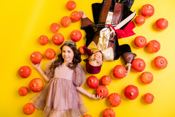 Above view portrait of two kids halloween princess pirate costume lying pumpkins isolated on yellow color background