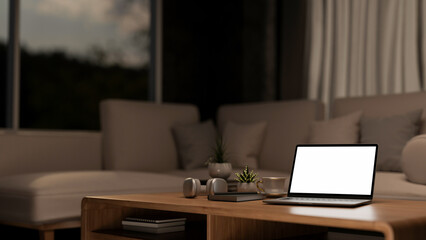 A laptop on a wooden coffee table in a comfortable contemporary living room at nighttime.