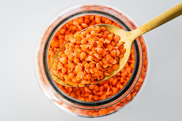 pantry staple close-up, spoonful of red lentils over clear glass jar shot from above