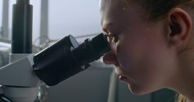 In medical laboratory, female microbiologist looks under microscope at samples, does analysis. Scientific method of research at work. Pharmaceutical discoveries. Development of medicine. Close up.