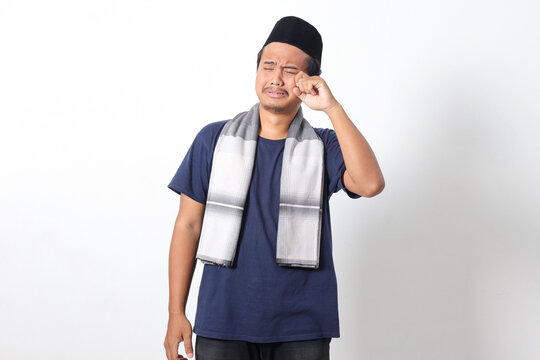 Portrait of suffering Asian muslim man wearing sarung scarf feeling timid, guy crying and looking upset, wiping tears and rub eyes depressed. Isolated image on white background