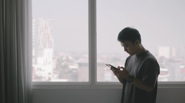 Young Asian man using a smartphone in the apartment with bokeh background