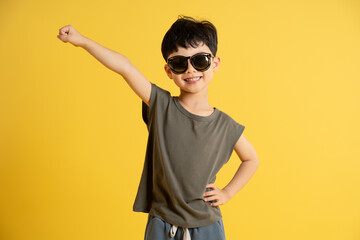 Portrait of asian boy wearing tank top and sunglasses posing on yellow background