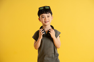 Portrait of an Asian boy wearing a tank top, headphones, and sunglasses posing on a yellow background