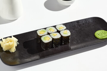 Minimalist Avocado Hosomaki Roll on Black Plate with Wasabi and Ginger in Bright Lighting