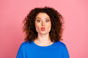 Charming young woman with red hair puckering lips in playful pose on pink background