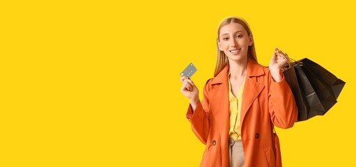 Beautiful happy young woman holding credit card and shopping bags on yellow background with space for text